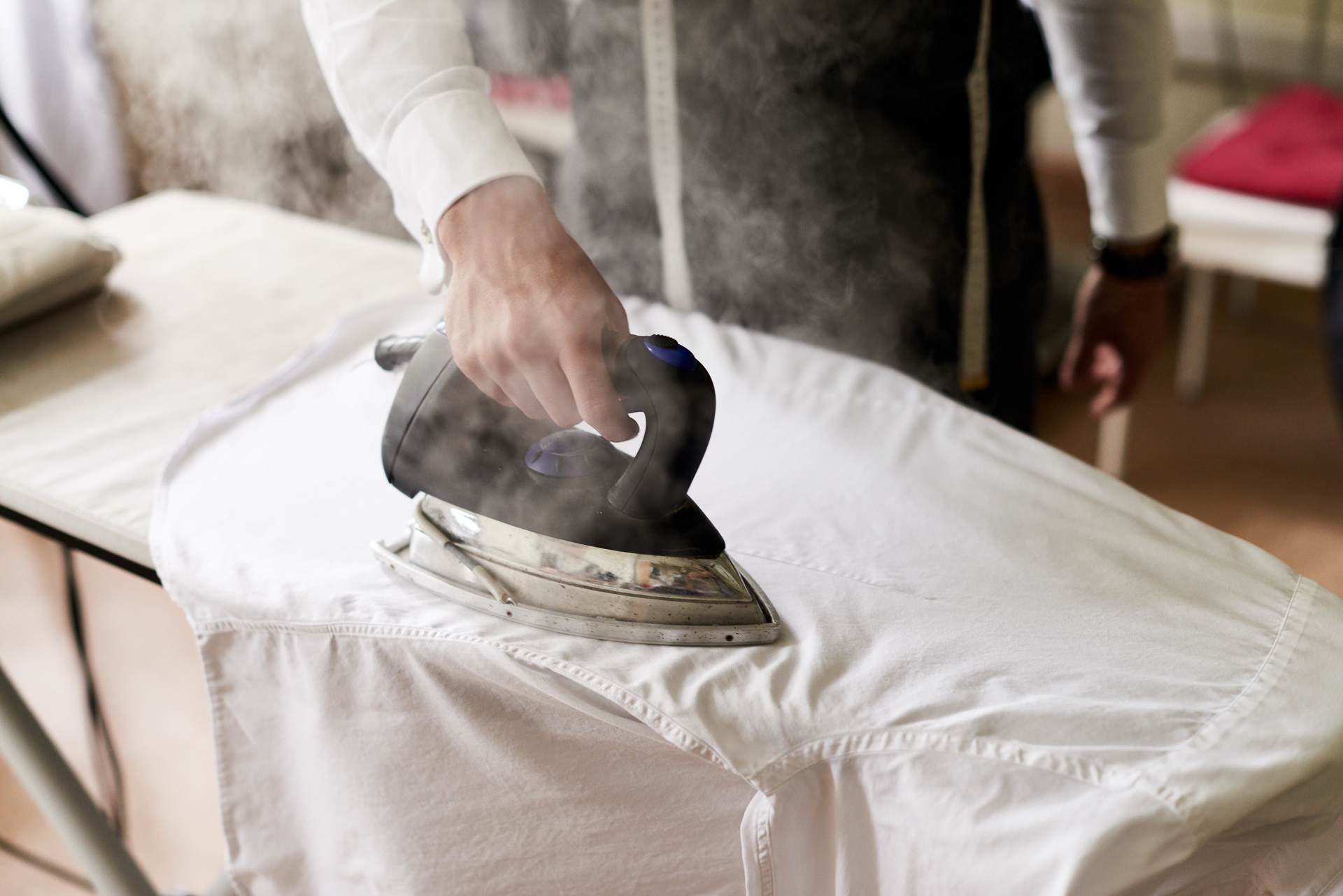 A person irons a white shirt with a steam iron, smoothing out wrinkles on an ironing board.