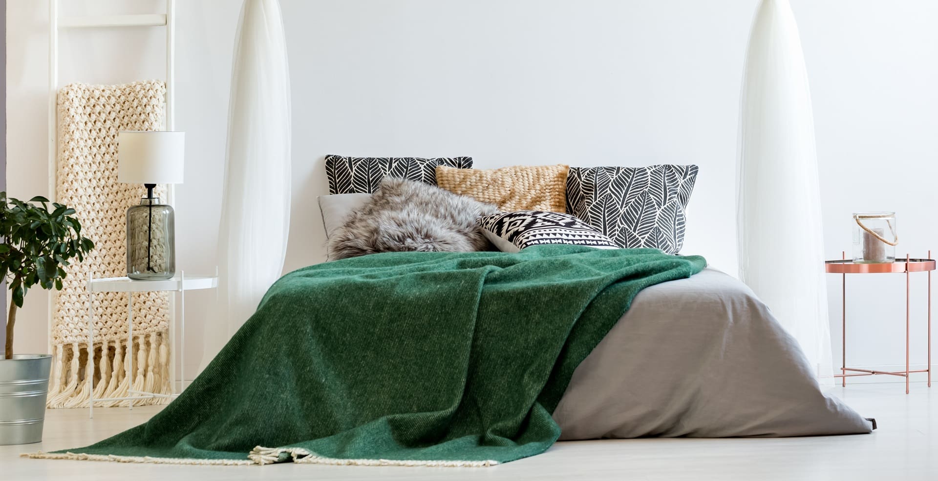 Cozy bedroom scene featuring a neatly made bed with a green blanket, decorative pillows, and a bedside table, representing Craft Cleaners' household items cleaning service for soft furnishings.