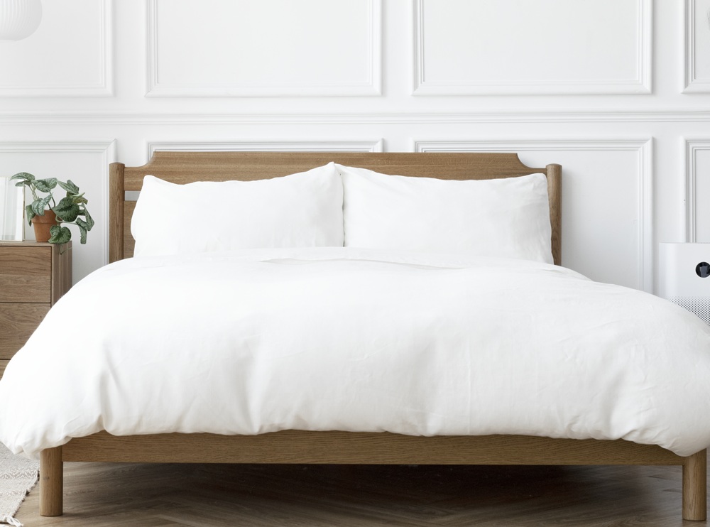 White bedding on a wooden bed frame in a bright, modern bedroom setting, highlighting clean and fresh linens for a welcoming home environment.