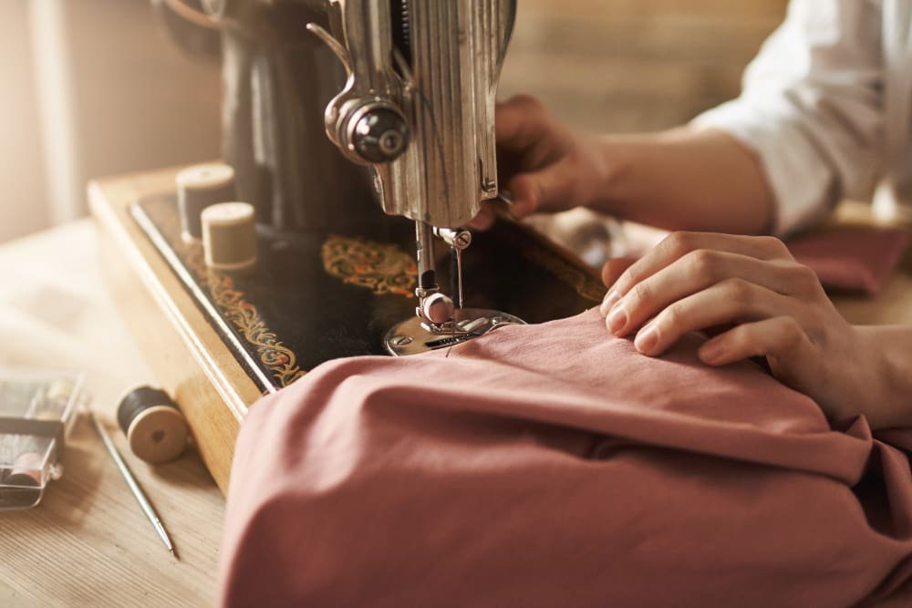 Sewing machine in use with hands adjusting pink fabric, illustrating Craft Cleaners' tailoring and clothing repair services.