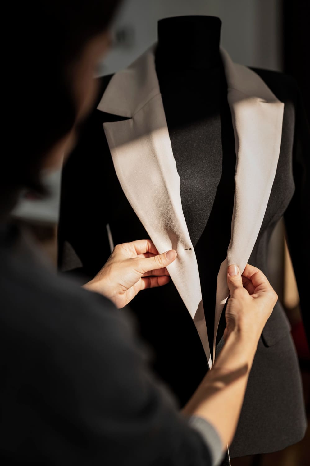 Person adjusting the collar of a tailored jacket on a dress form, demonstrating clothing alteration techniques relevant to Craft Cleaners' tailoring services.