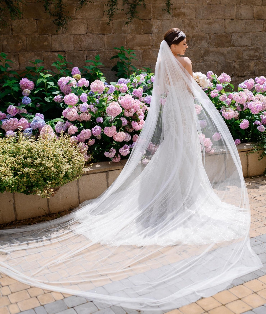 Bride in elegant wedding dress with flowing veil, standing among blooming hydrangeas, showcasing craftsmanship and beauty, symbolizing cherished memories and preservation services by Craft Cleaners.