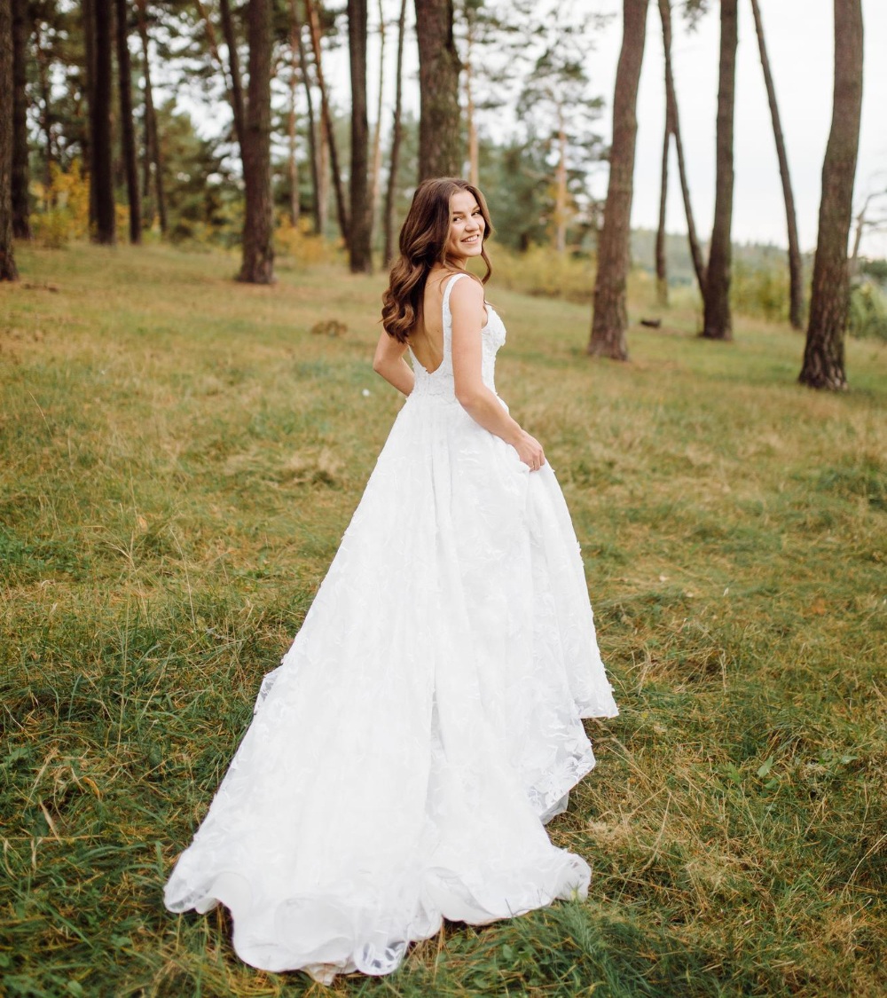 Bride in a flowing white wedding dress with lace details, standing in a forested area, showcasing the elegance of wedding gown preservation by Craft Cleaners.