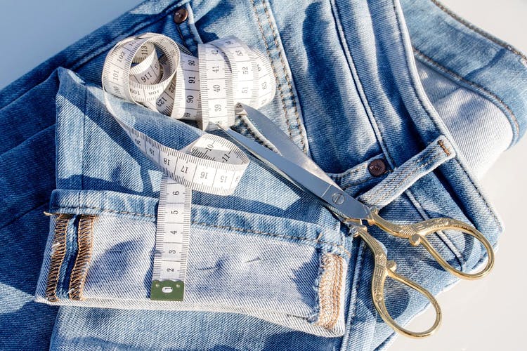 Scissors and measuring tape on a pair of denim jeans, illustrating tailoring and customization for best-fitting jeans.