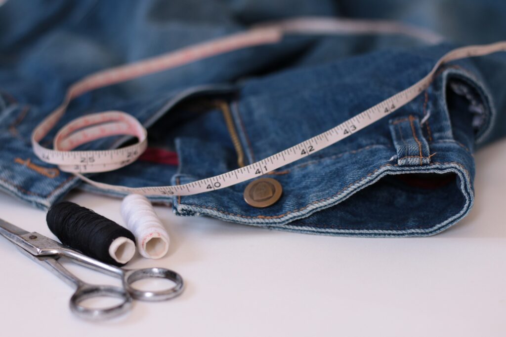 Denim jeans with measuring tape, scissors, and spools of thread, symbolizing professional tailoring services for custom-fit alterations at Craft Cleaners.