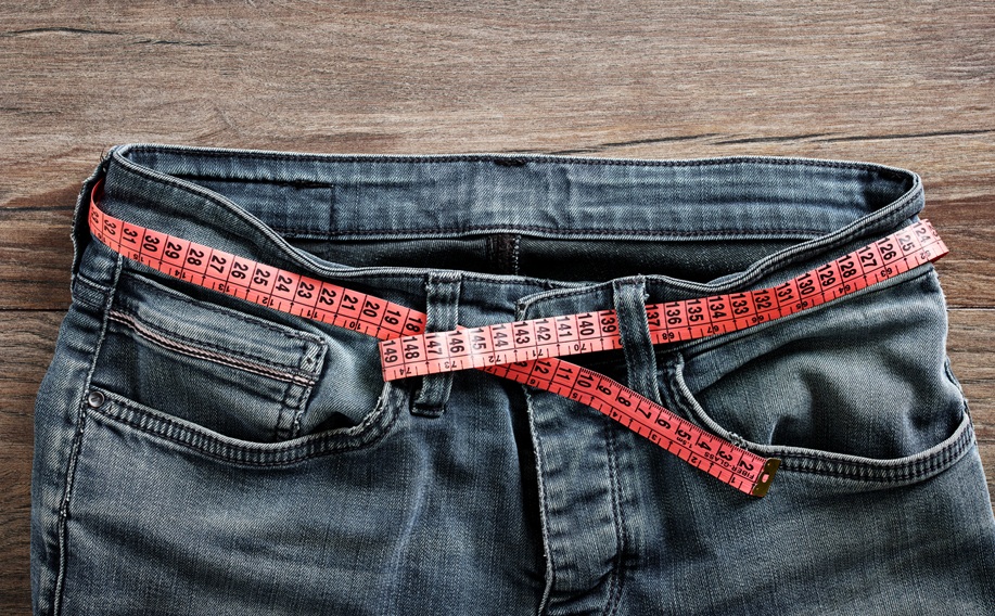 Jeans with a measuring tape wrapped around the waistband, illustrating custom alterations for a perfect fit.