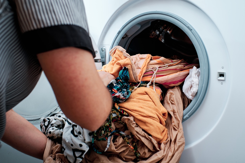 Person loading a washing machine with a mix of colorful clothing, emphasizing laundry care and household management.