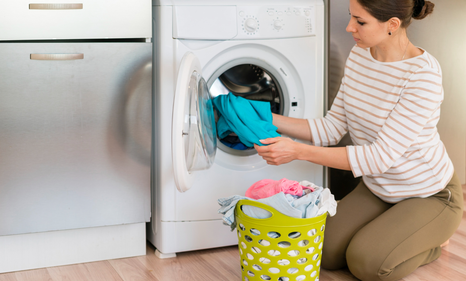 Woman loading laundry into a washing machine, with a green laundry basket filled with clothes nearby, illustrating home laundry care.
