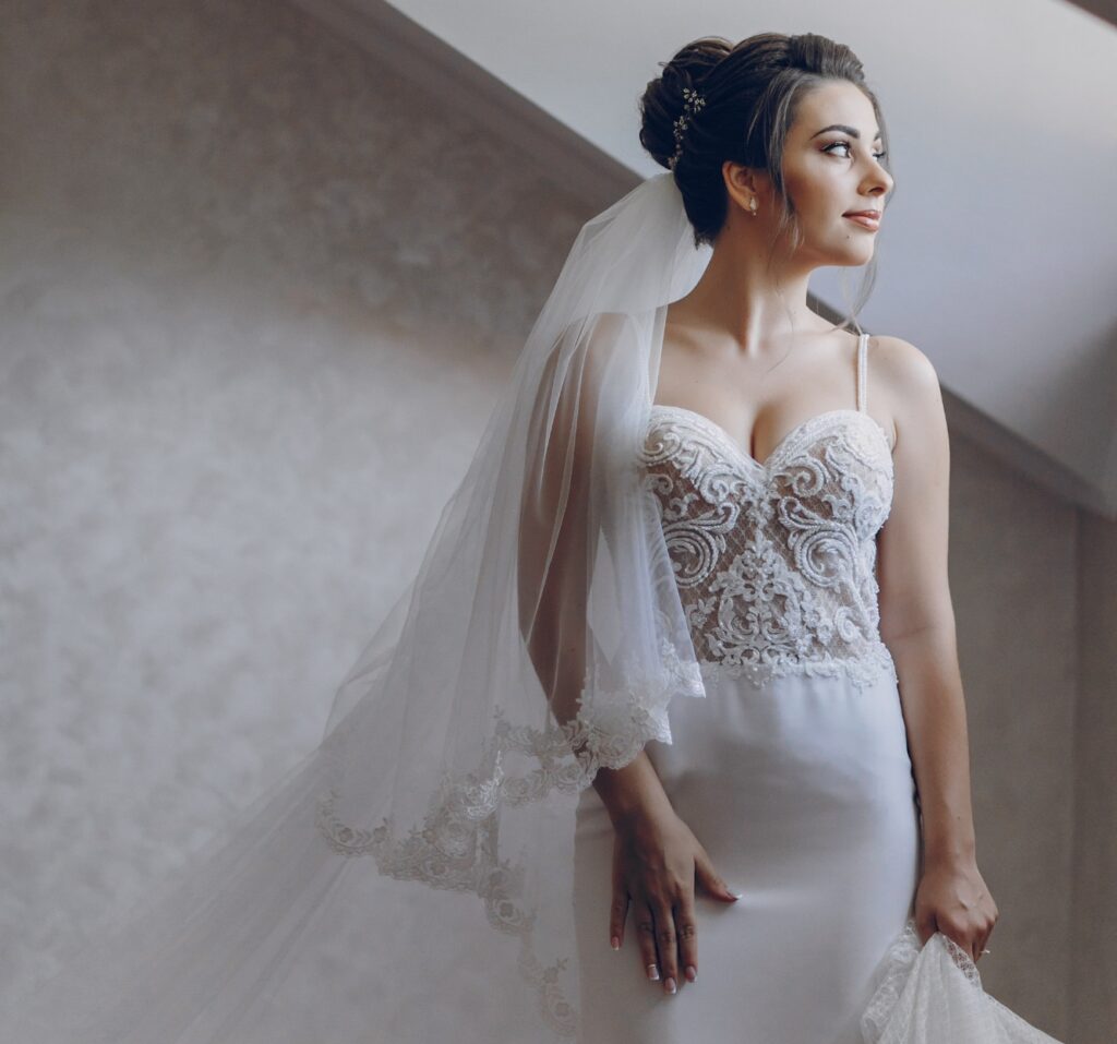 Bride in elegant wedding dress with intricate lace detailing and flowing veil, preparing for the wedding day, symbolizing bridal attire care and preservation by Craft Cleaners.